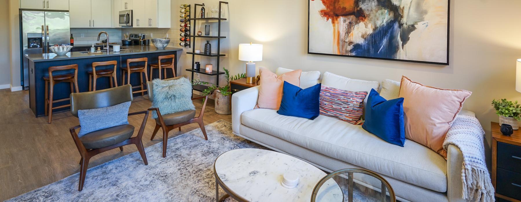 a living room with a couch and chairs and kitchen beyond it